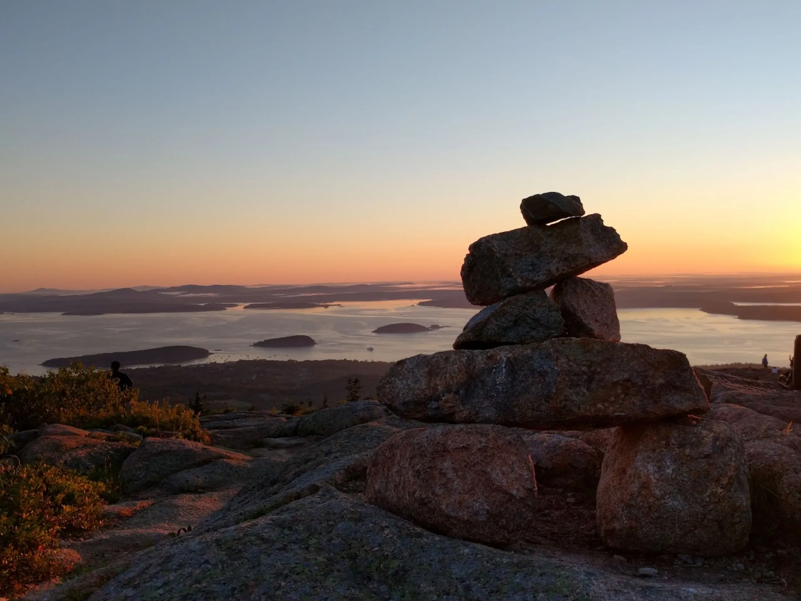 A stacked stone cairn on a headland above the sea at sunrise